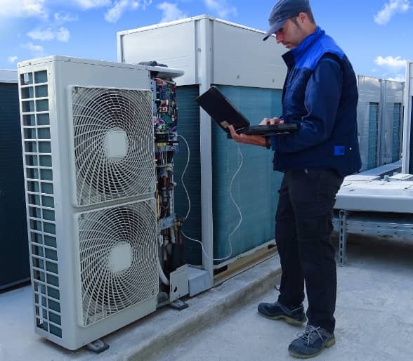 Un technicien en uniforme diagnostique la climatisation commerciale sur le toit d'un édifice à l'aide de son ordinateur portable