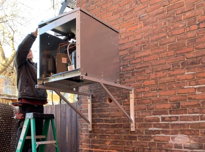 Technicien en train d'installer une unité de climatisation sur un mur en brique extérieur